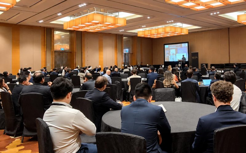 Wide shot of an audience seated at round tables listening to a keynote presentation at the MAPS by BluFin conference in a large ballroom.