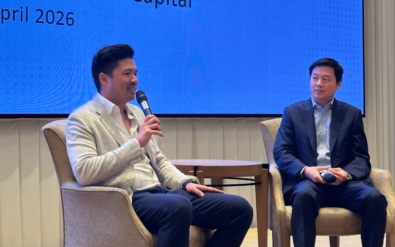 Two business leaders seated on stage during a private event discussion, with one speaker holding a microphone in front of a presentation screen referencing Pantera Capital.